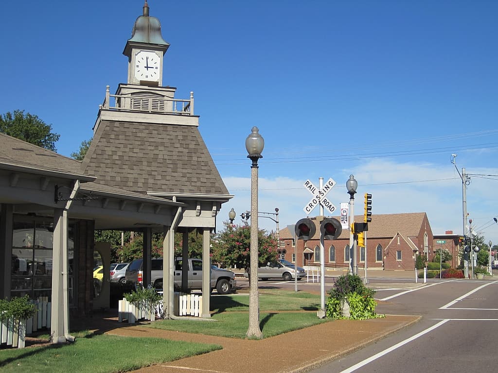 The clock tower pavilion and railroad crossing in Old Town Bartlett, Tennessee, with a brick church across Stage Road