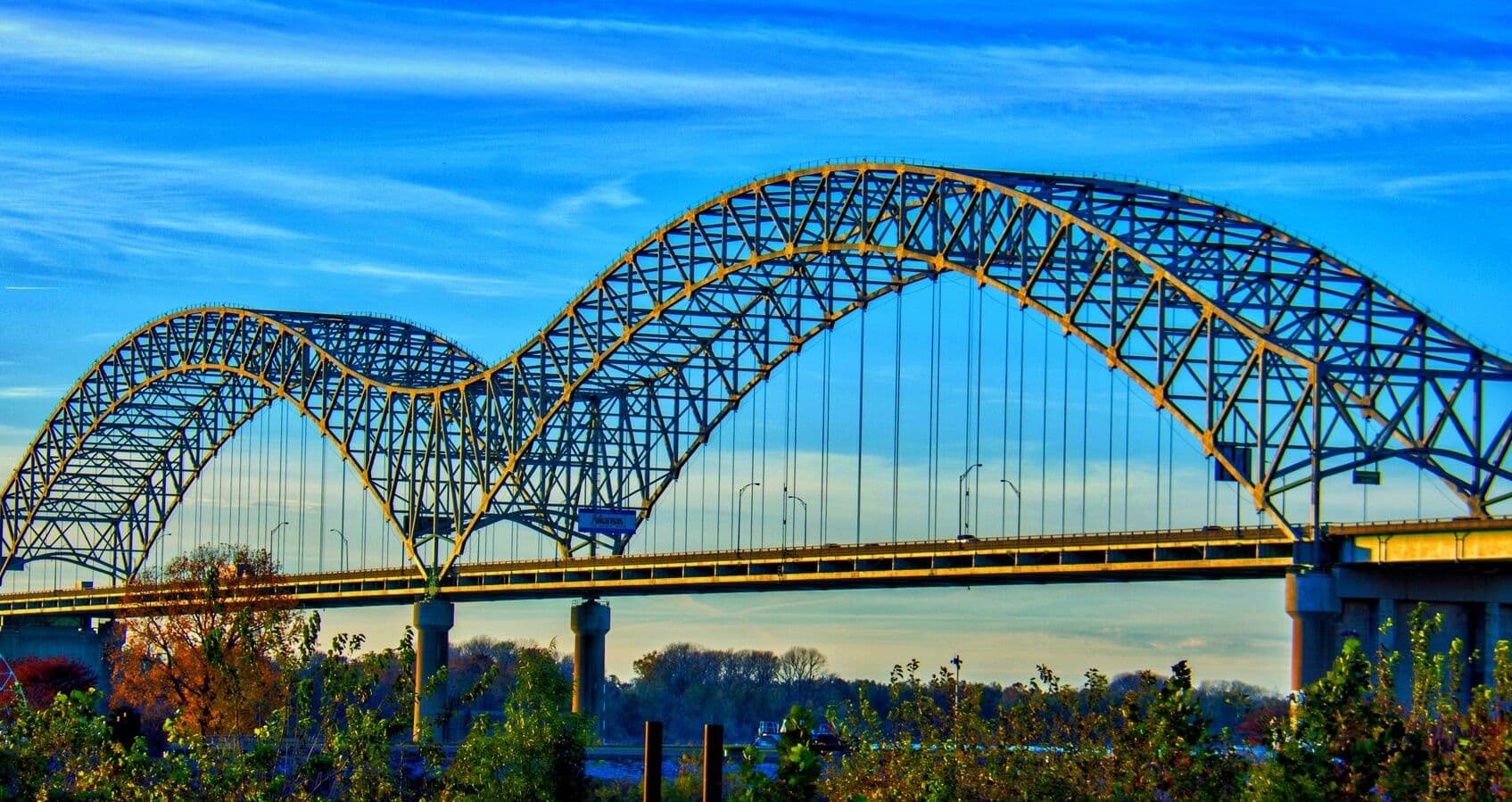 The Hernando de Soto Bridge — the double steel arch that carries I-40 over the Mississippi into Memphis — catching late sun against a bright blue sky